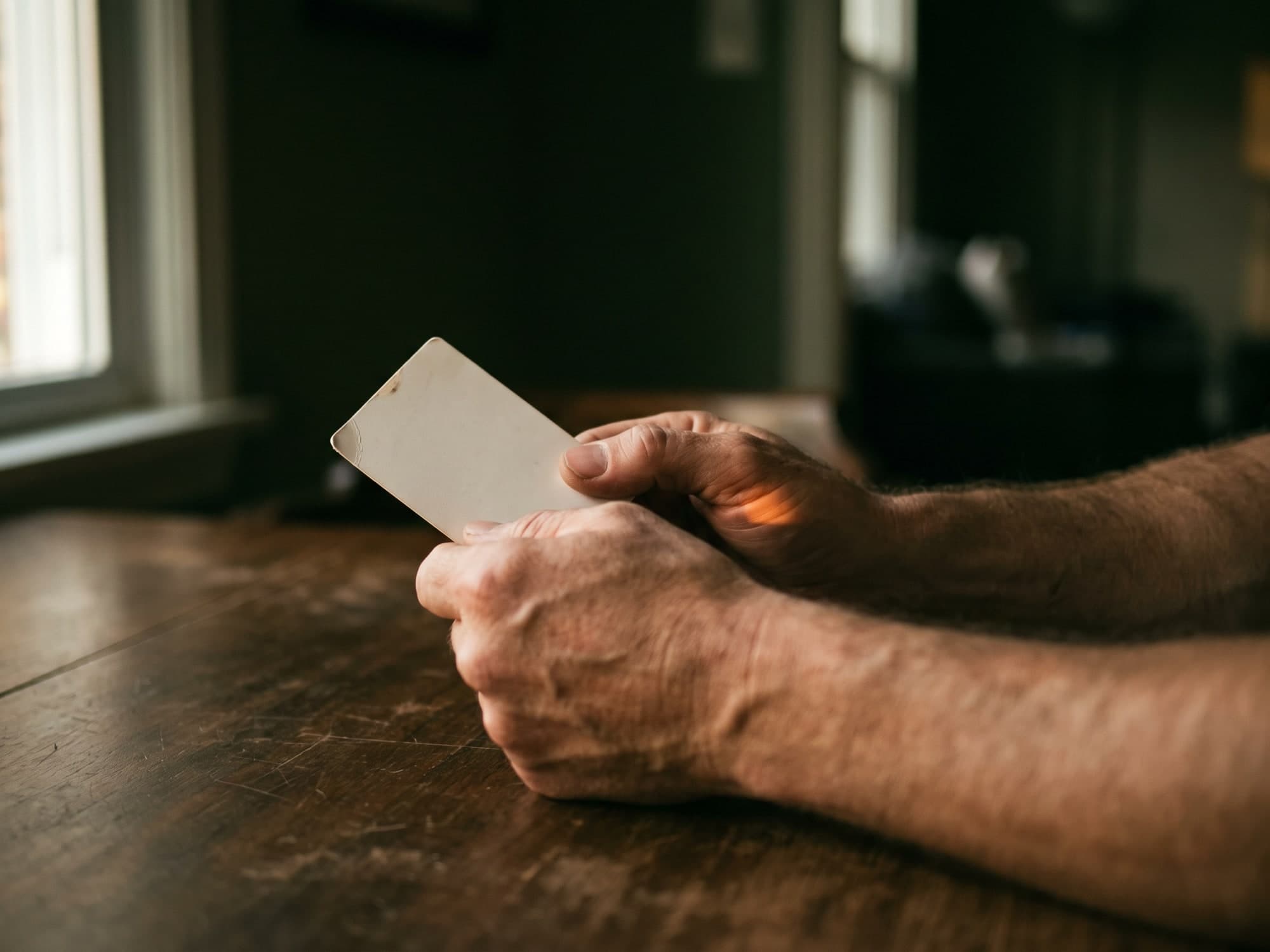 Two hands holding a small printed card at a table in evening light.